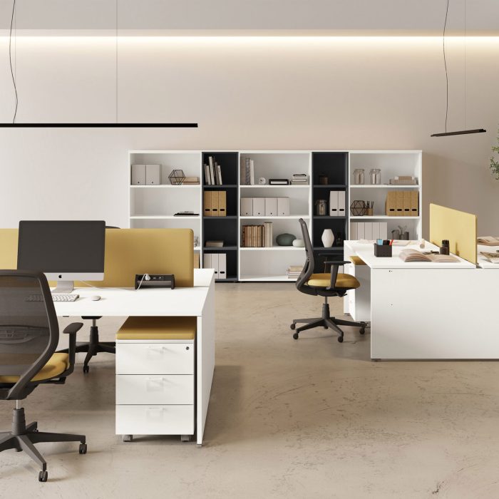 Nowoczesne biuro typu open space z białymi biurkami i żółtymi panelami akustycznymi. Na pierwszym planie białe biurko z czarnym krzesłem obrotowym i monitorem, a w tle biały regał z segregatorami oraz zielone rośliny doniczkowe.